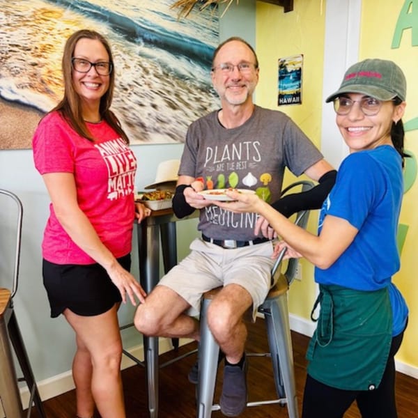 Three smiling people, two customers and one staff member, holding a healthy food plate at Leahi Health.