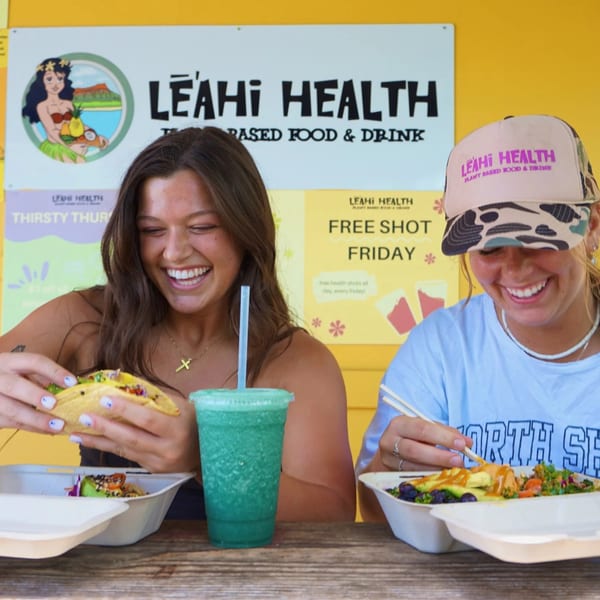 Two smiling women enjoying healthy tacos, a smoothie, and a bowl at Leahi Health.